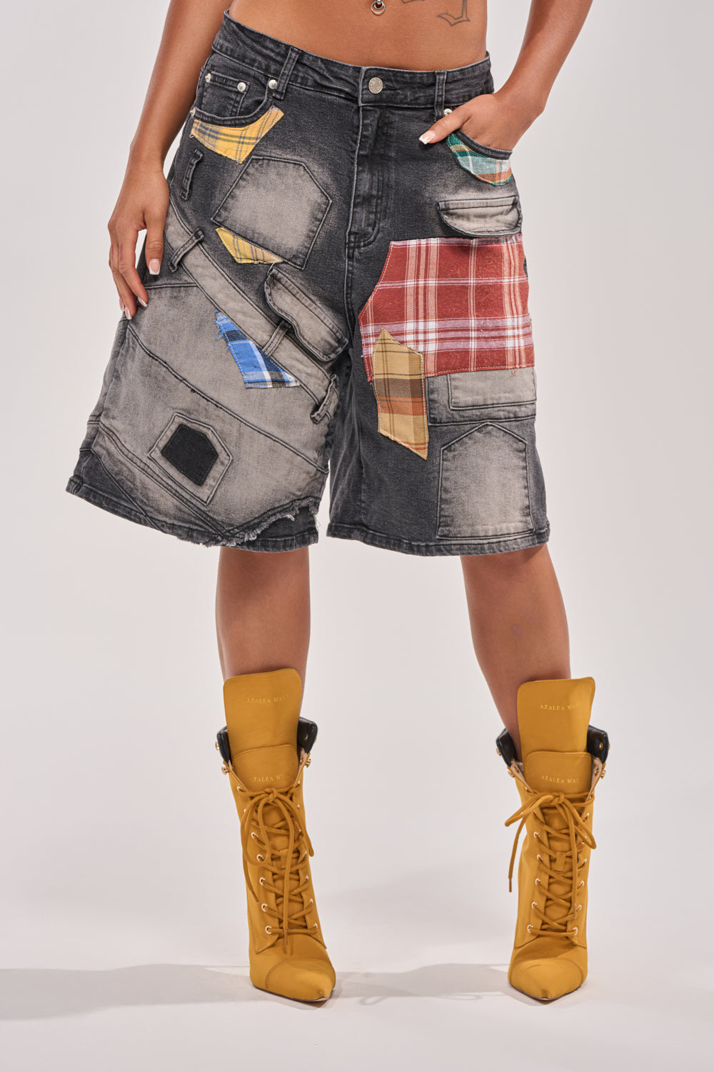 Wearing the DREA MIXED PLAID BERMUDA SHORT, featuring black denim with colorful plaid and solid fabric patches, and paired with yellow lace-up ankle boots for an effortless street style look. 2