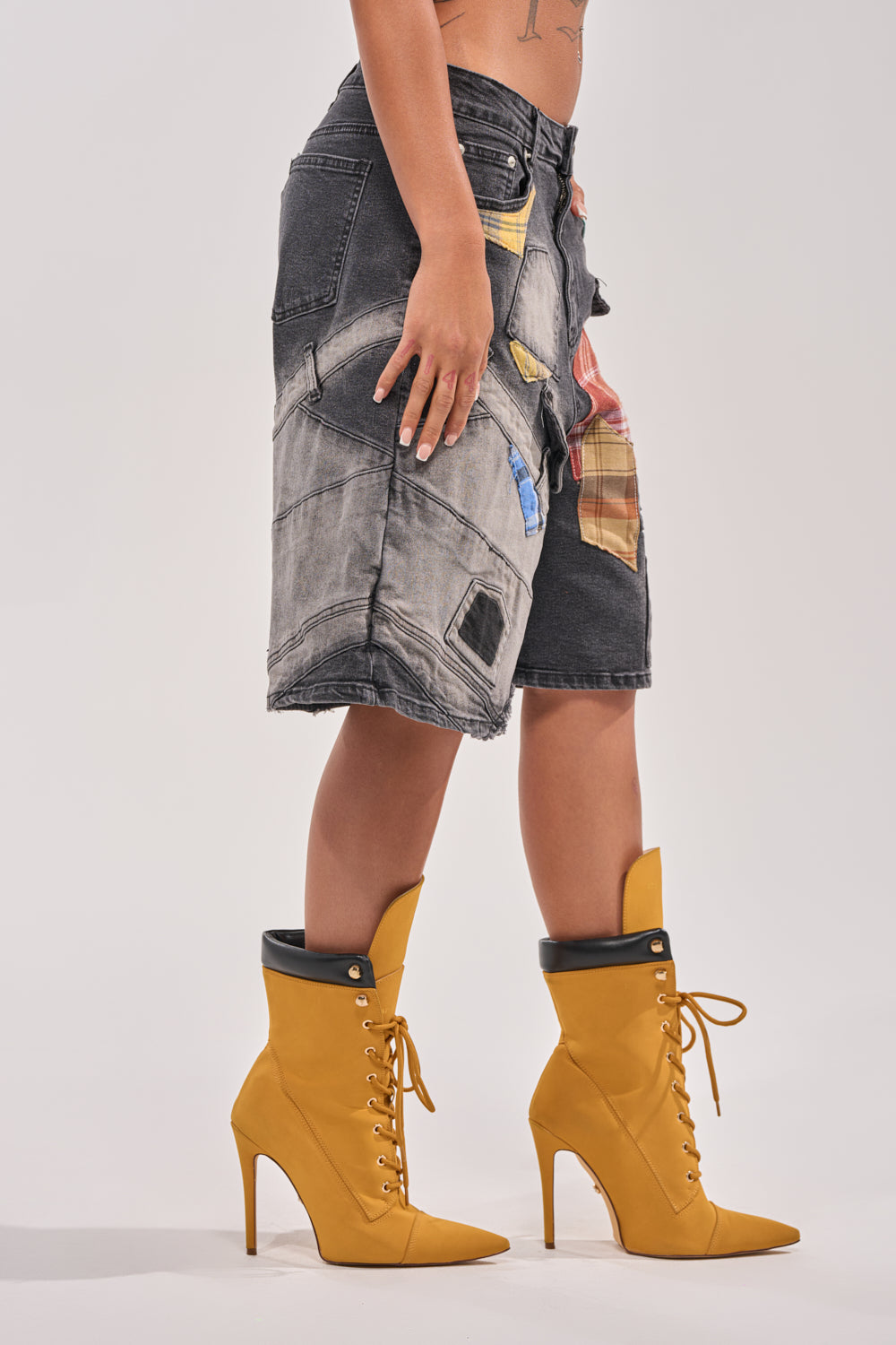 A person wearing DREA MIXED PLAID BERMUDA SHORTS and mustard yellow, lace-up high-heeled boots with black trim stands on a white background. 3