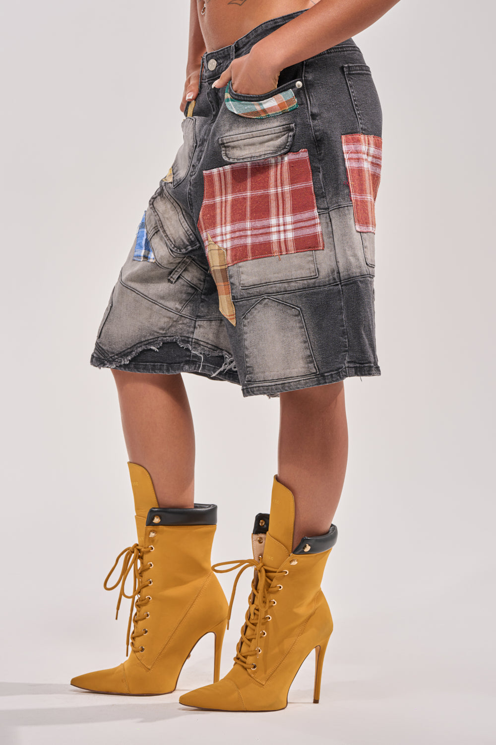 A person showcases bold street style by wearing the DREA MIXED PLAID BERMUDA SHORT—knee-length patchwork denim shorts with plaid patterns—teamed with mustard yellow lace-up high-heeled boots. 4