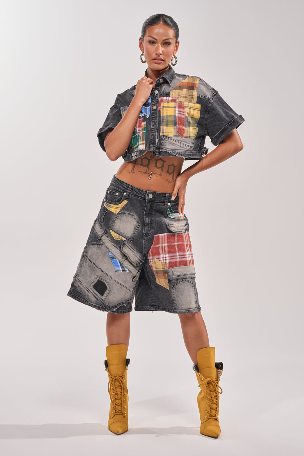 A woman poses confidently in the DREA MIXED PLAID CROP SHORT SLEEVE BUTTON DOWN and matching shorts with colorful plaid patches, paired with yellow heeled boots, her hair slicked back against a light background. 4