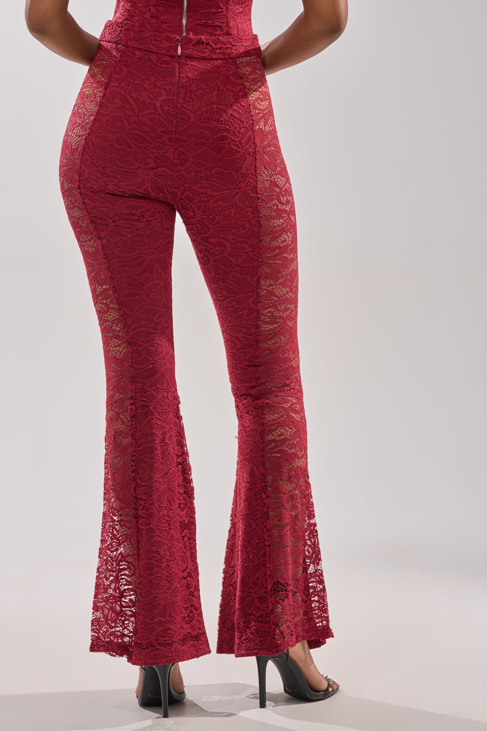 A person in high-waisted red LOVE BOMB LACE PANT and black high heels, shown from the back against a plain light background.