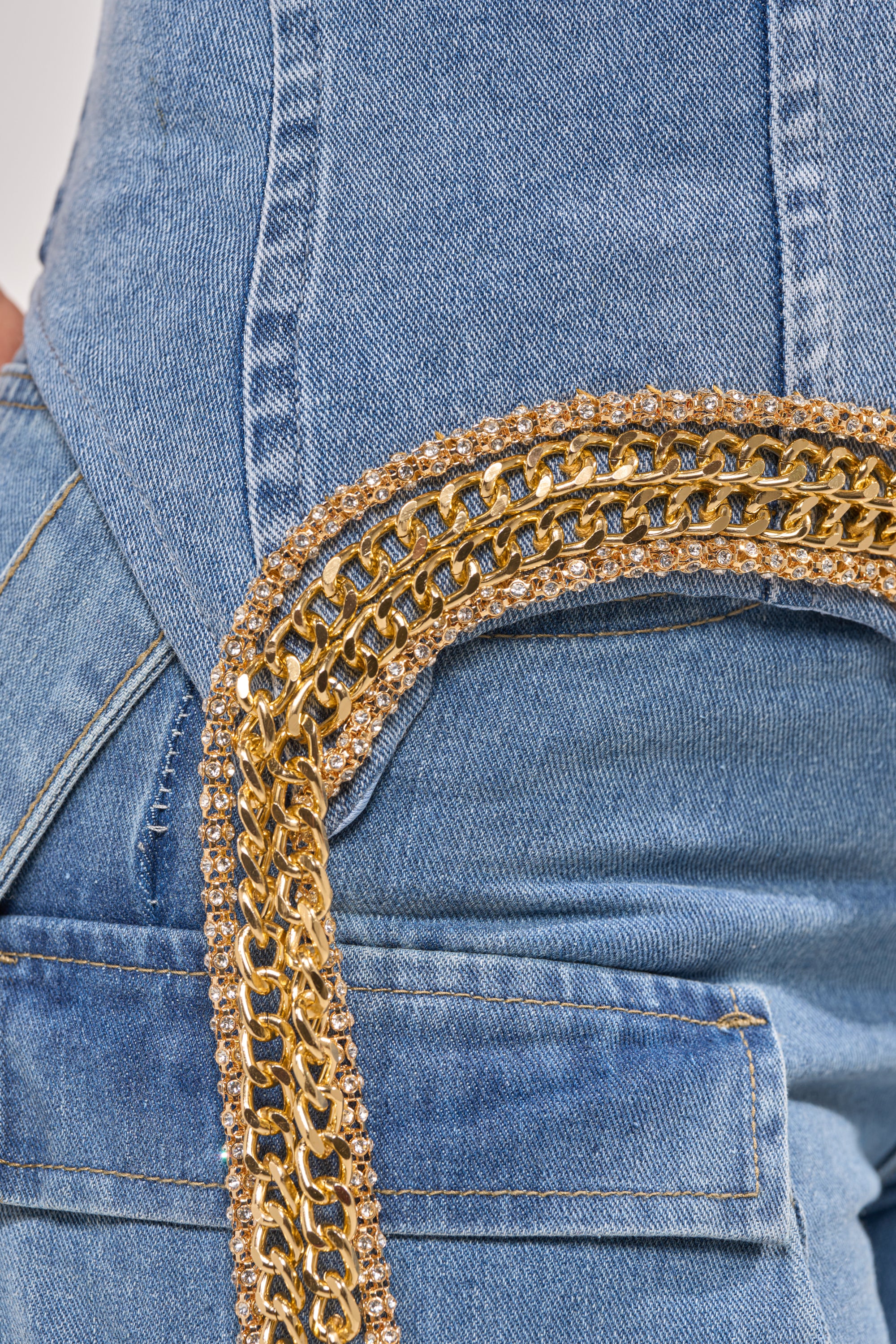 Close-up of a person wearing the SHOW IT OFF DENIM CORSET with blue denim jeans and a shiny gold chain fringe trim draping from the corset’s waistband to the back pocket. 7