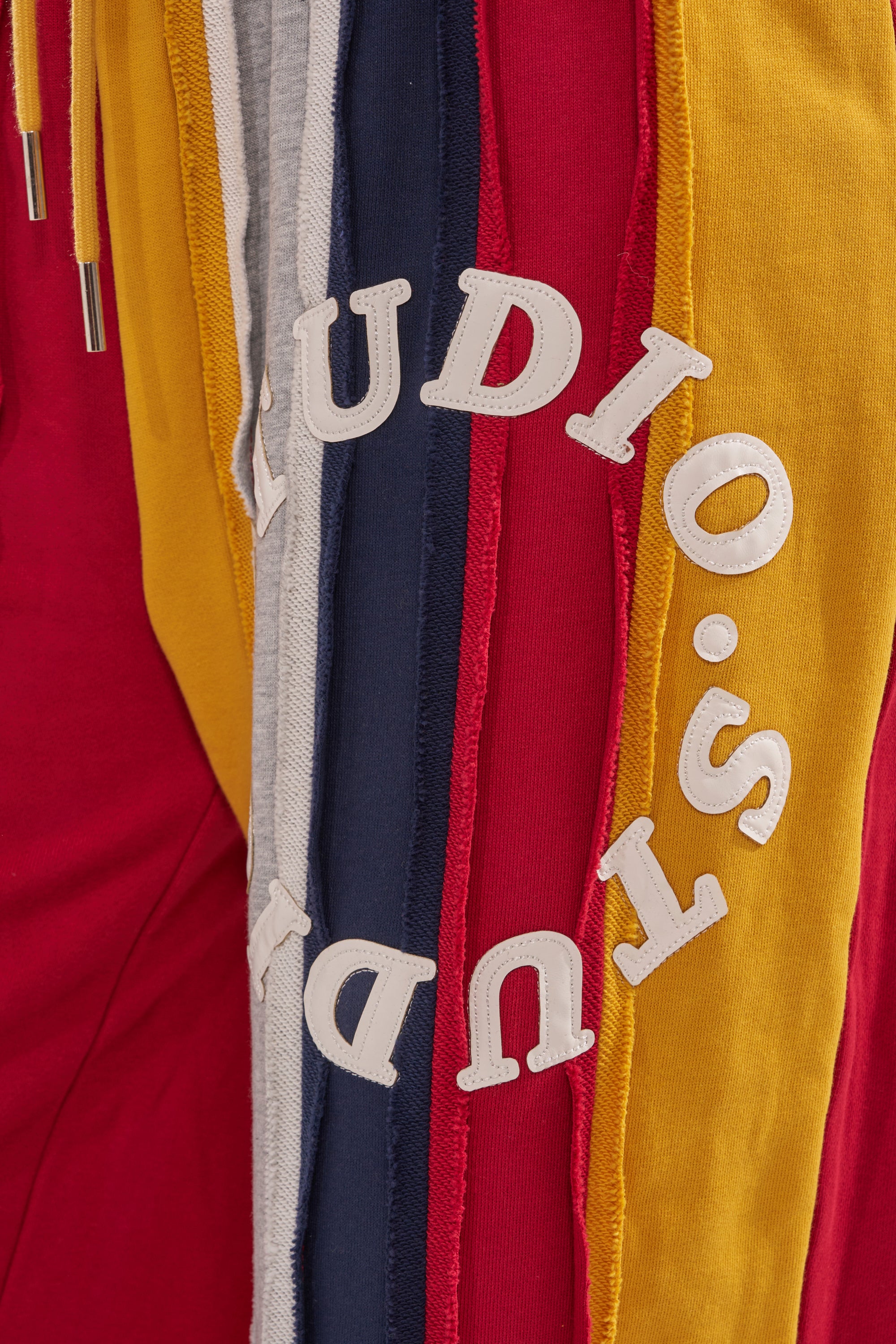 A close-up of the STUDIO LIVING JOGGER shows red, yellow, gray, and navy fabric strips layered like patchwork with partially visible white "STUDIO" letters across the folds. 6