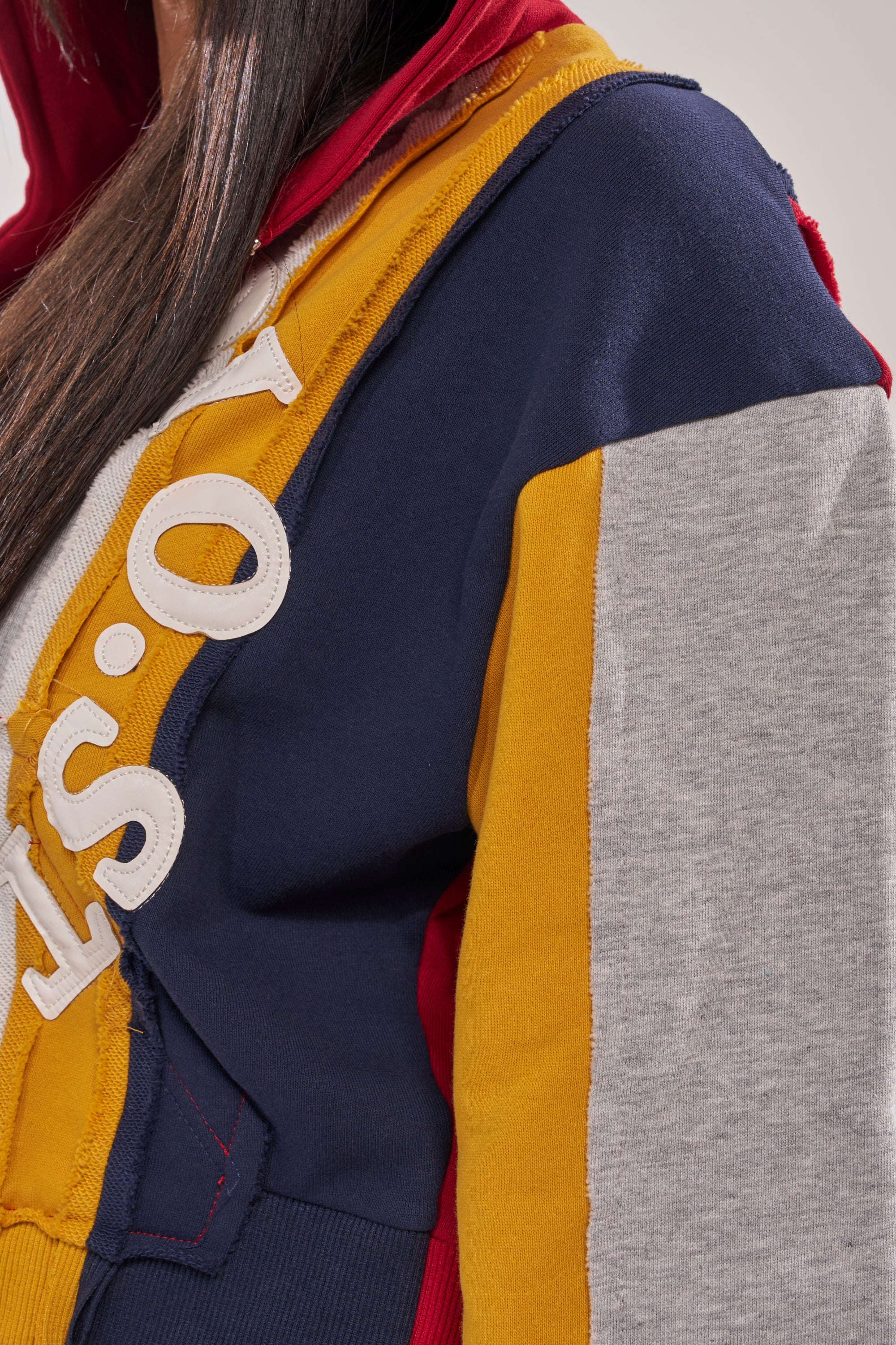 Close-up of a person wearing the STUDIO LIVING SWEATSHIRT, a color-blocked hoodie with navy, yellow, red, and gray panels, bold white letters, and visible stitching—ideal for standout streetwear style. 9