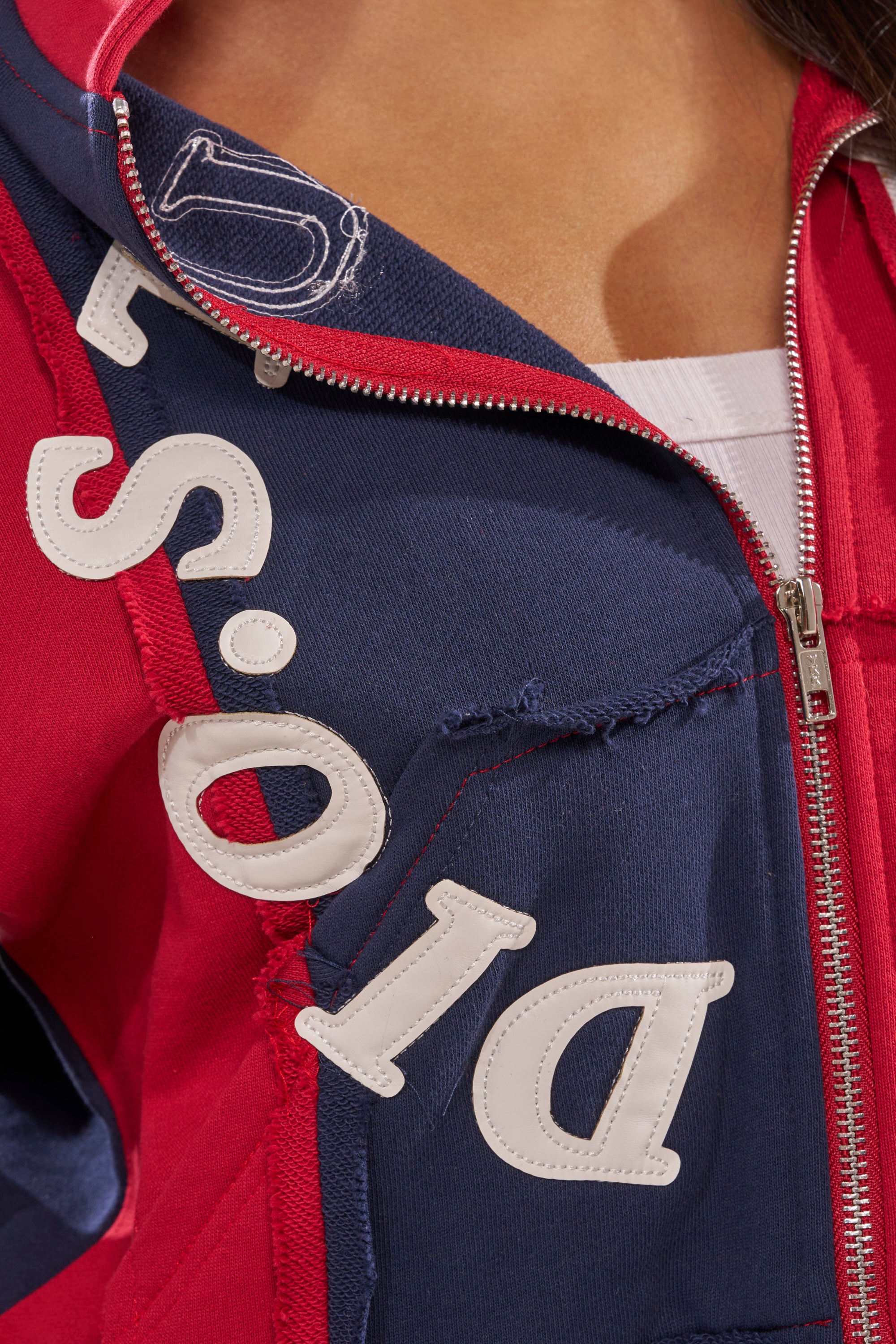 Close-up of a person wearing the STUDIO LIVING SWEATSHIRT, a red and navy streetwear zip-up with frayed edges and bold diagonal "DIOR" lettering, partially unzipped to show a white shirt underneath. 8