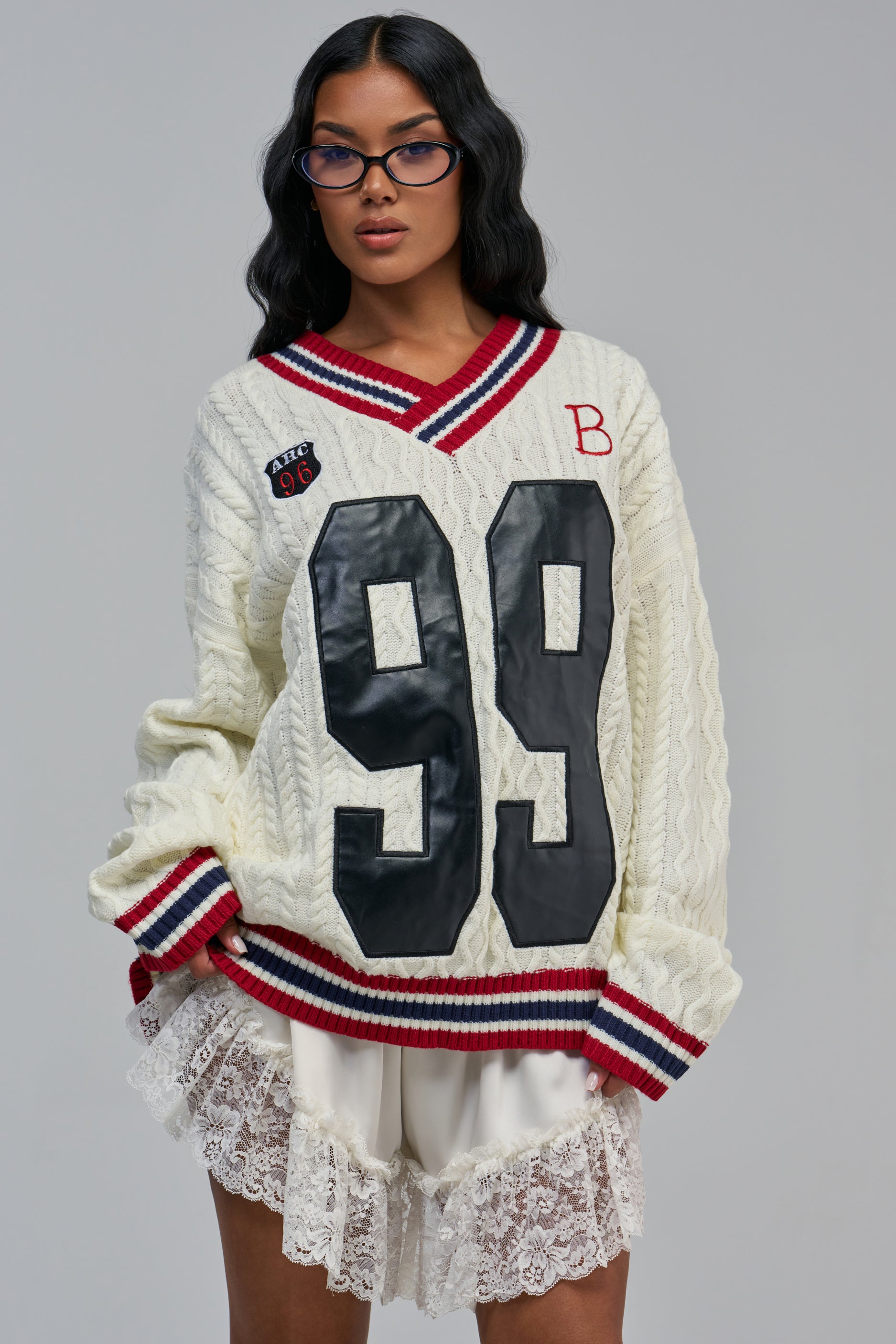 IVY LEAGUE ENERGY SWEATER: a cream-colored preppy cable-knit varsity sweater with navy and red striped trim, a large black “99” on the chest, an “ABC 96” patch, and a red “B” monogram.