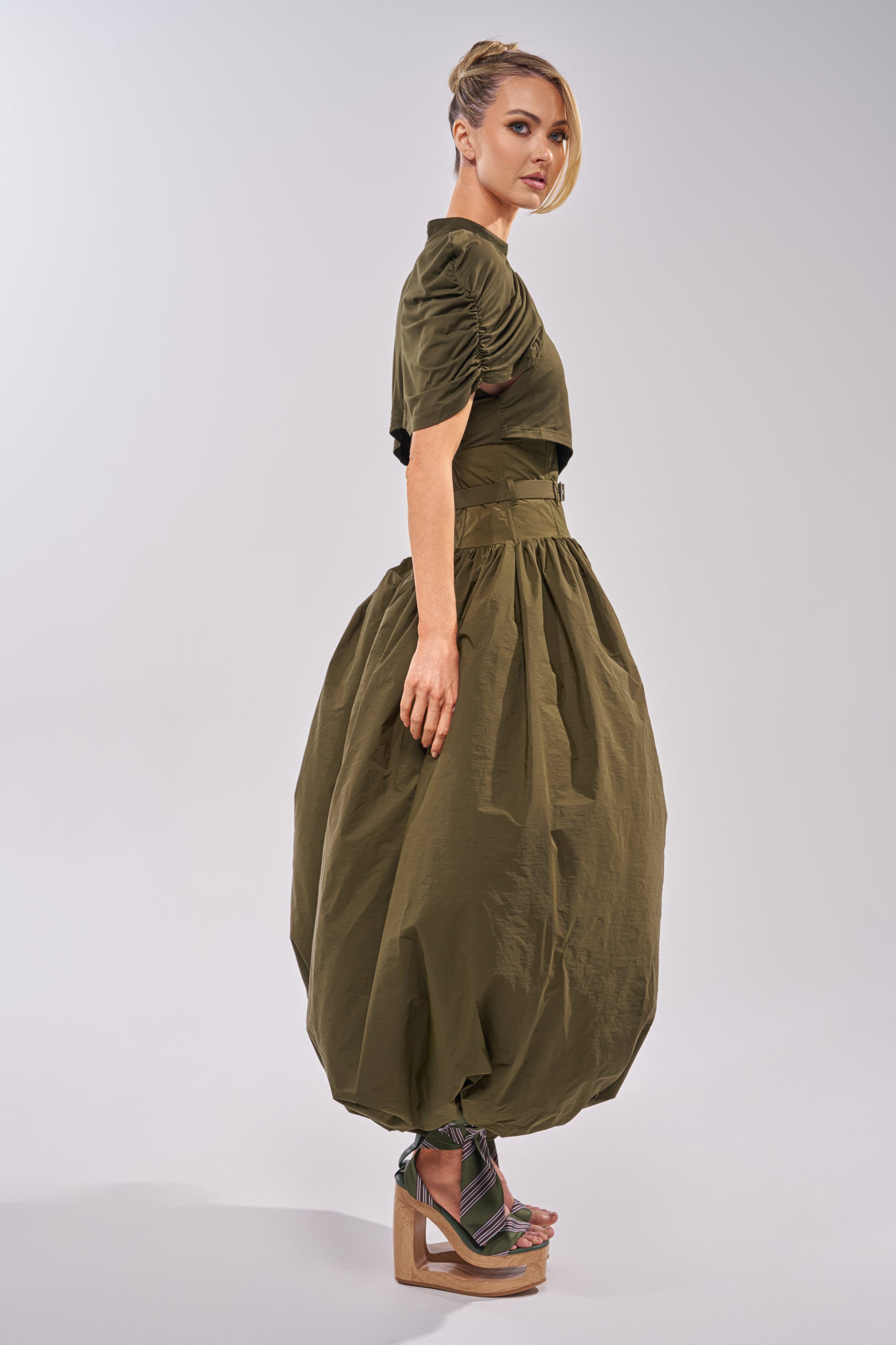 A woman in profile wears the SPIN ME AROUND POPLIN JUMPSUIT with balloon-shaped legs. Her hair is styled up, and she pairs it with strappy wedge sandals against a plain, light-colored background. 5