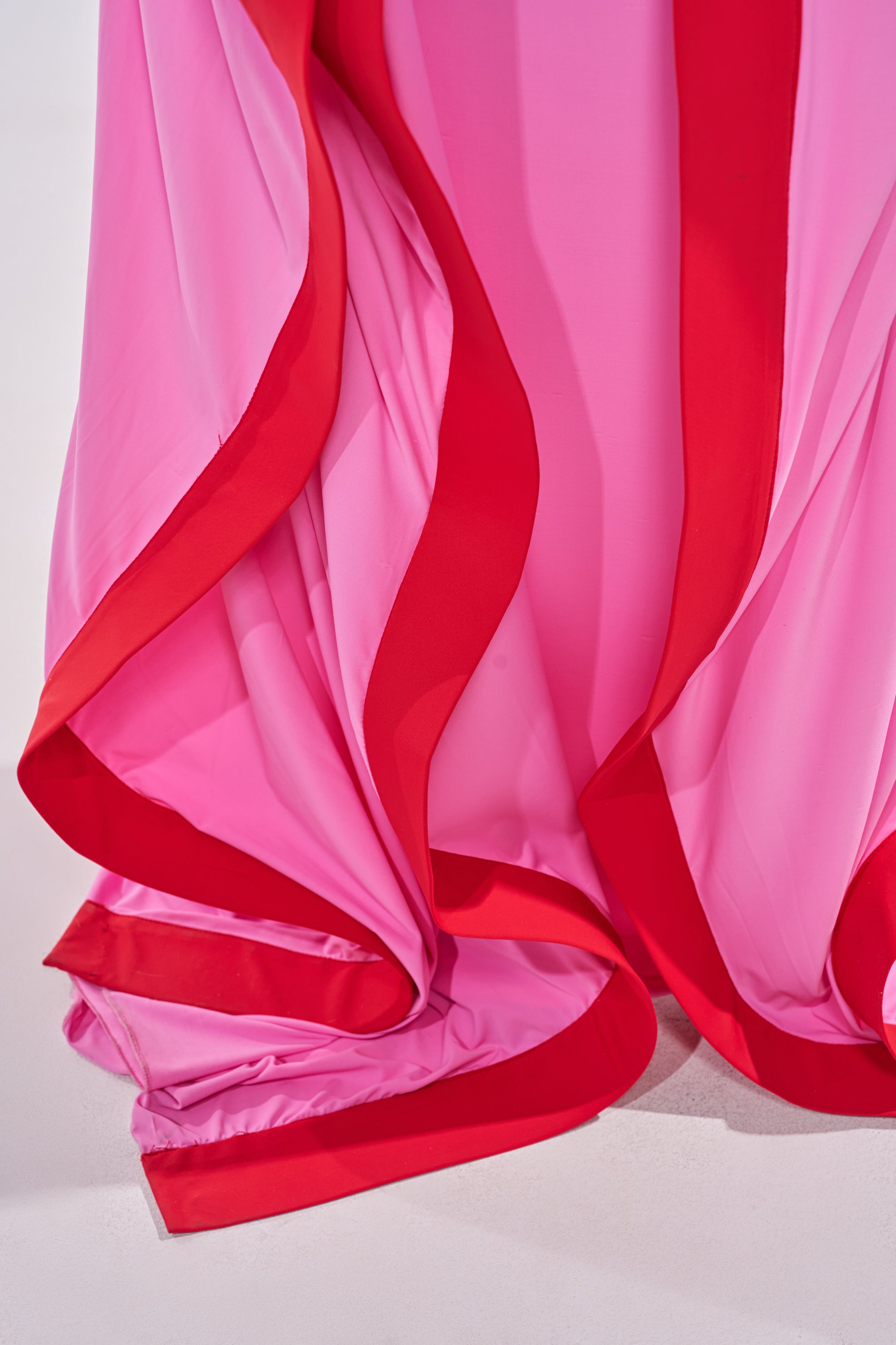 Close-up of the GUEST OF HONOR BODYCON MAXI DRESS IN PINK, featuring flowing pink fabric with bold red edges and elegant gathered folds, creating a soft, wavy look and vibrant contrast. 6