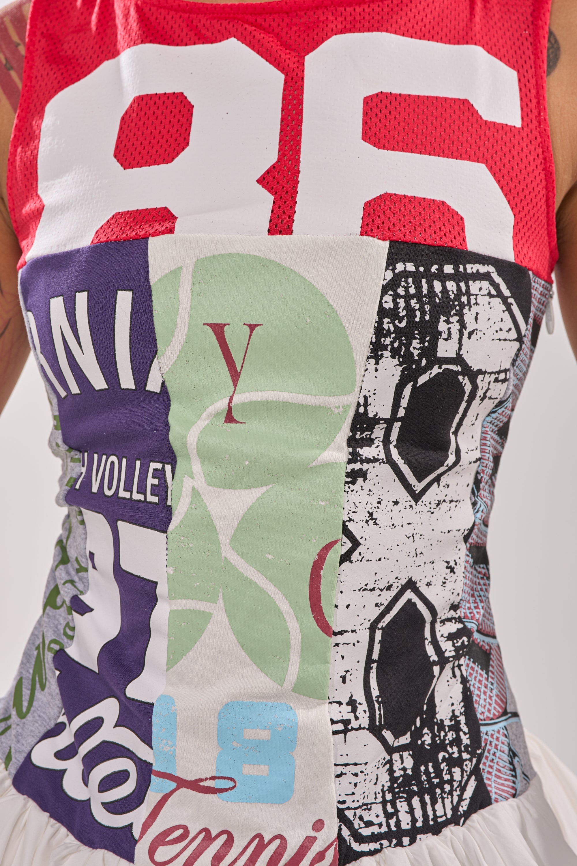 A close-up of a torso wearing the TEAM SPIRIT BUBBLE MINI DRESS, a colorful patchwork piece inspired by sports jerseys with large numbers, letters, and bold prints in red, green, black, and white. 11