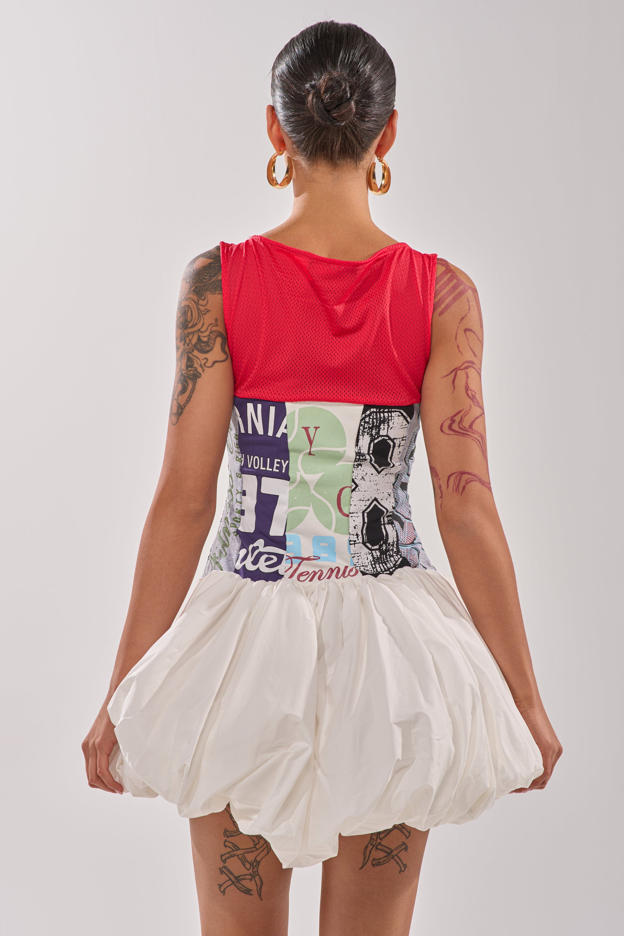 A person with tattooed arms, seen from behind against a plain light background, wears a red sleeveless top and the TEAM SPIRIT BUBBLE MINI DRESS. 8