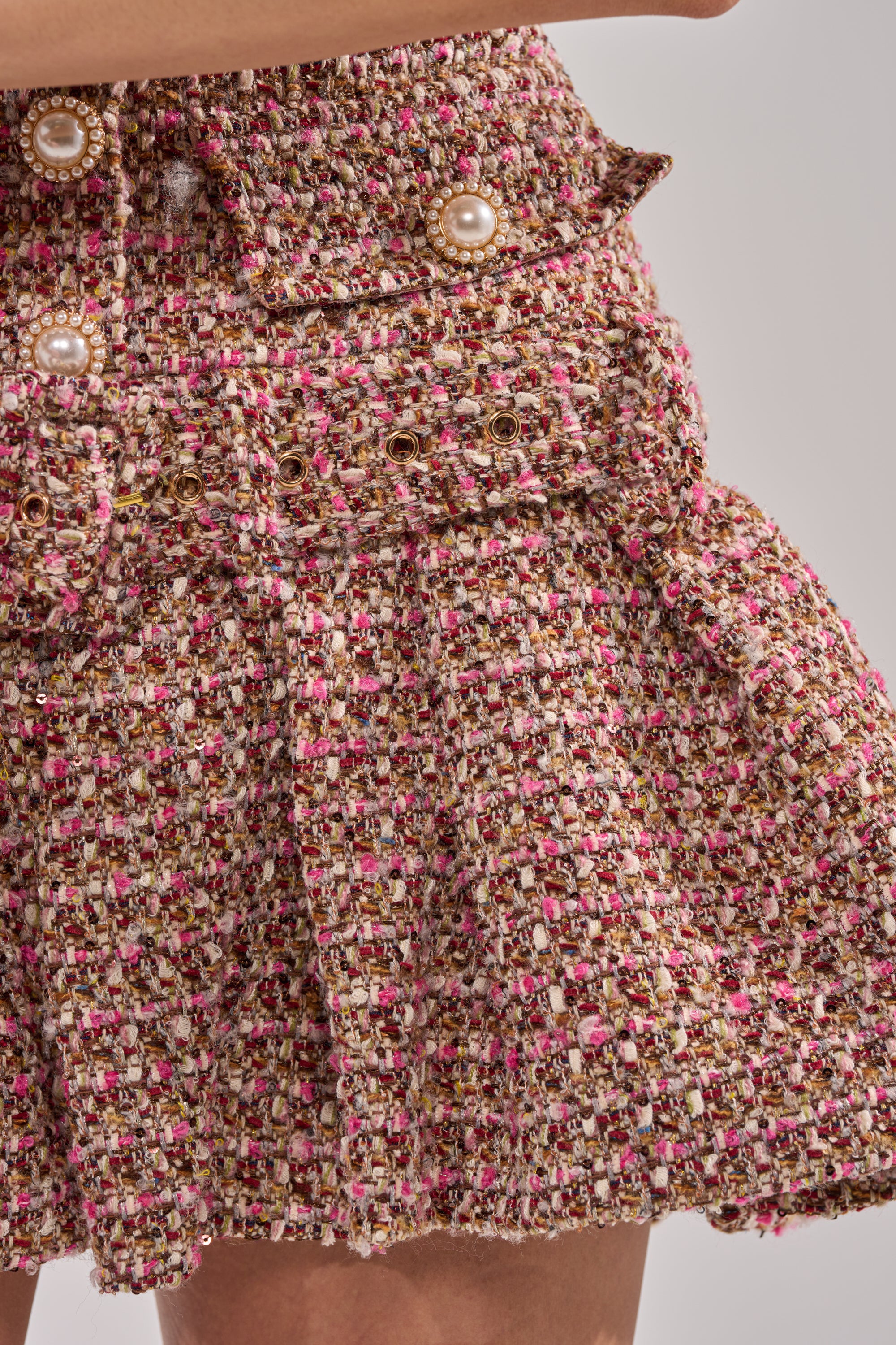 Close-up of the SWEET CAROLINE MINI TWEED DRESS in pink, gold, and white tweed with decorative pearl buttons and a fitted waist, worn by a person with light skin. 7