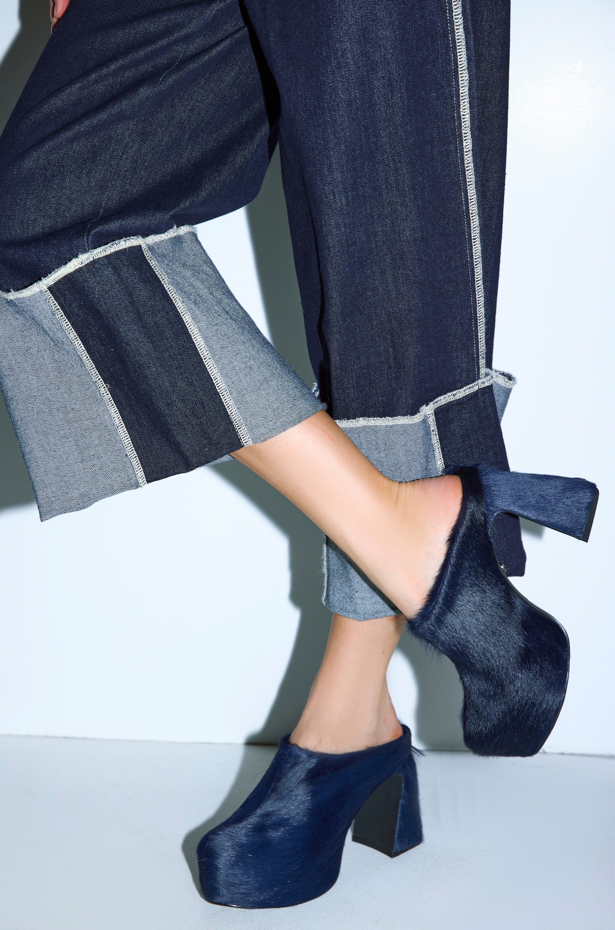 A person in wide-leg, dark denim pants with frayed cuffs pairs them with AZALEA WANG GOLDING NAVY PONY HAIR CHUNKY PUMP shoes, standing against a white background. 2