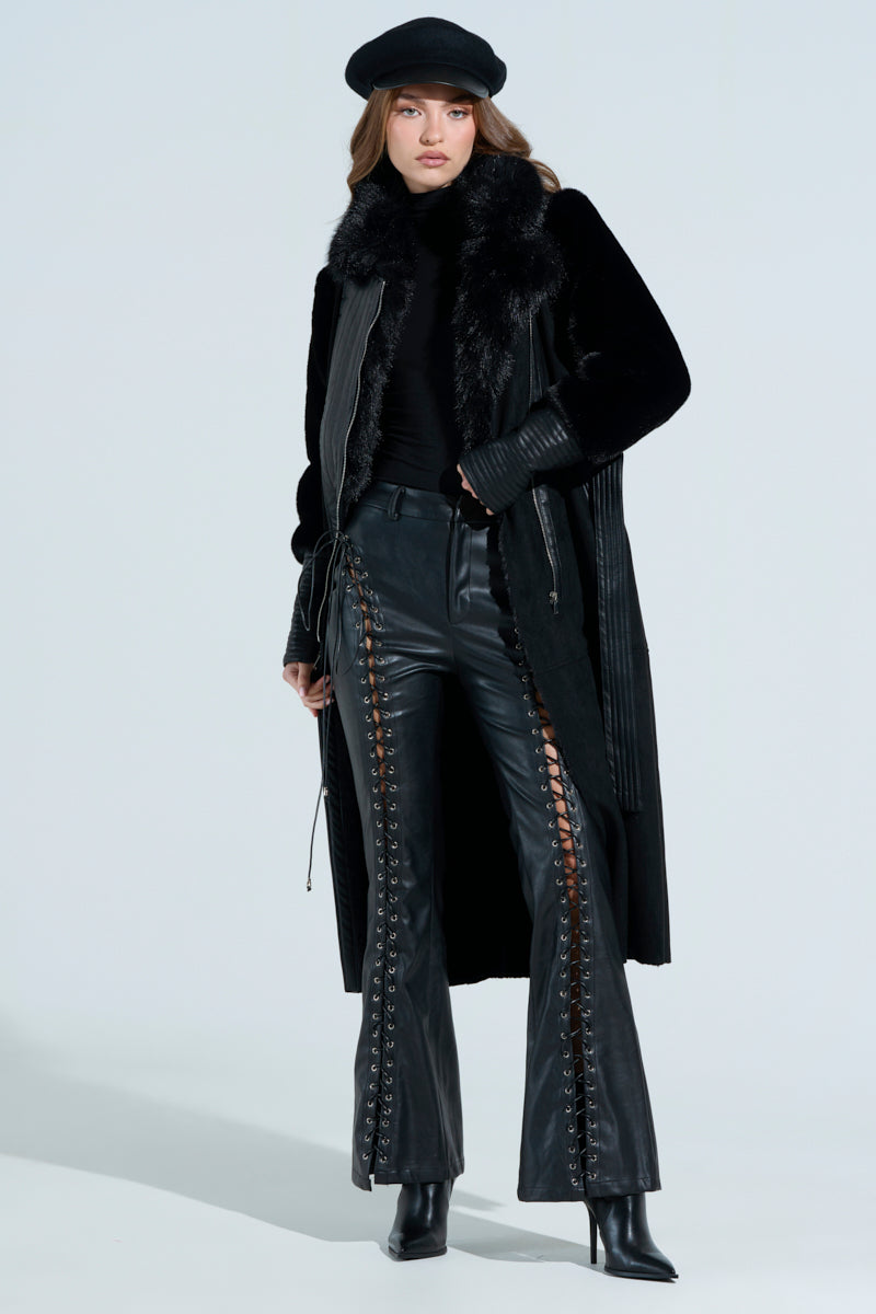 A person wears a black outfit featuring the GOODIE MIXED MEDIA COAT with faux fur trim, a turtleneck top, lace-up leather pants, and heeled boots. They complete the look with a black beret and pose confidently against a plain background.