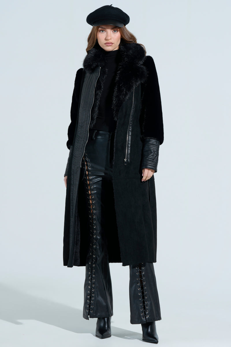 Sporting a sleek and stylish ensemble, the individual dons the GOODIE MIXED MEDIA COAT with faux fur trim, paired with a black beret and vegan leather pants featuring lace-up detailing against a light background.