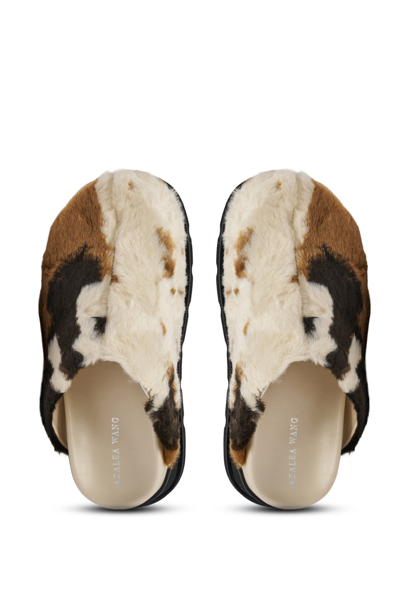 The AZALEA WANG GOVINDA MULTI SLIP ON COW PRINT CLOG features brown, white, and black faux fur uppers, black soles, and beige insoles in a comfortable slip-on design, shown from an overhead view.