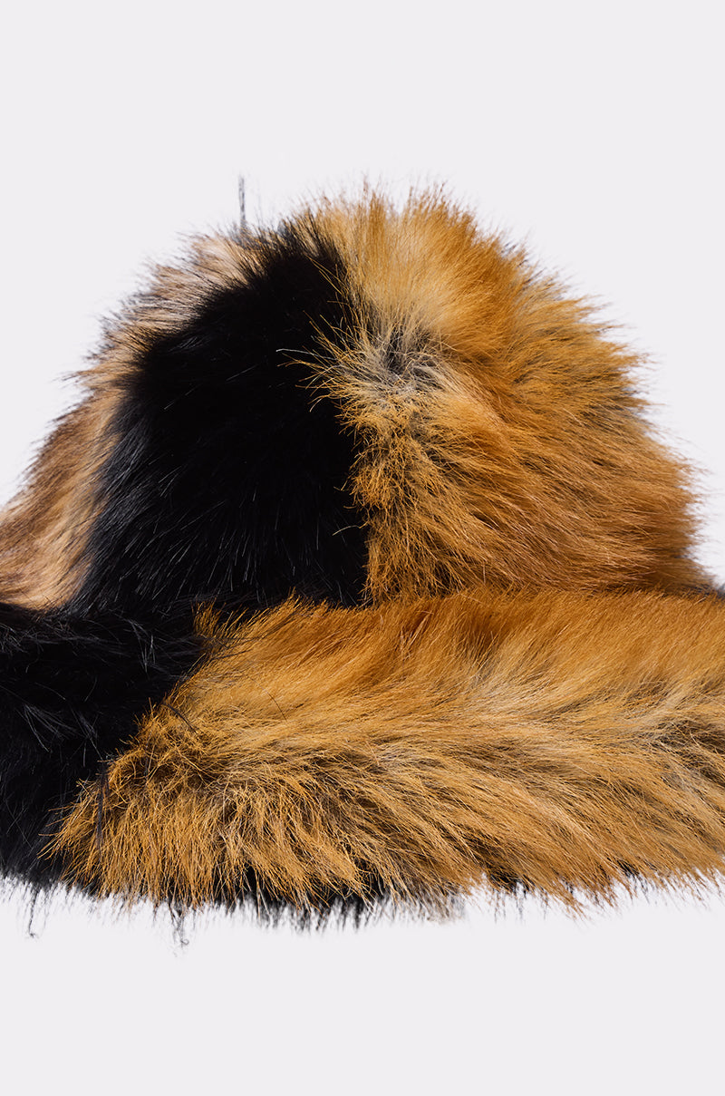 The COSMO FAUX FUR OVERSIZED BUCKET HAT features long, black and golden brown faux fur in a patchwork pattern, offering a bold and cozy statement for cold weather.