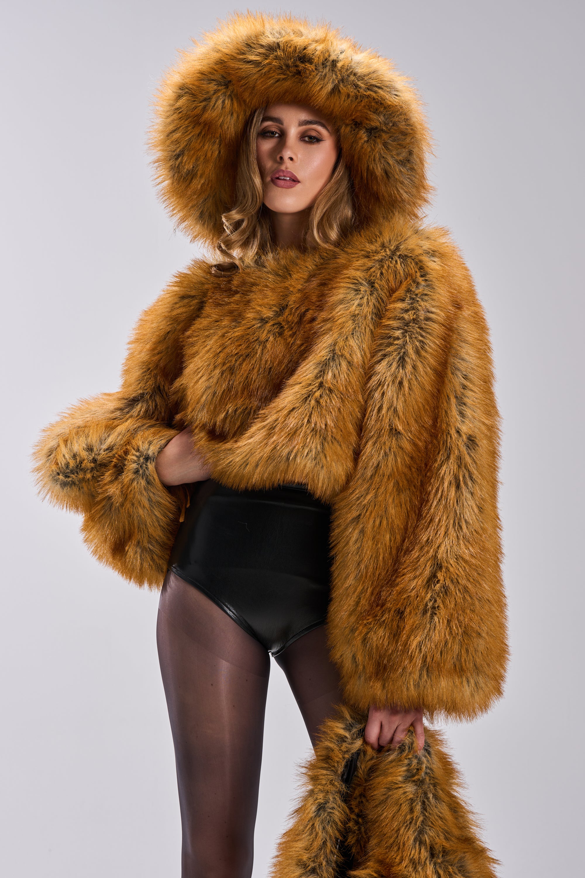 A person confidently poses against a gray background, wearing the HOT GIRL FAUX FUR OVERSIZED BUCKET HAT with a matching fluffy orange faux fur coat, black high-waisted bottoms, and sheer black tights.