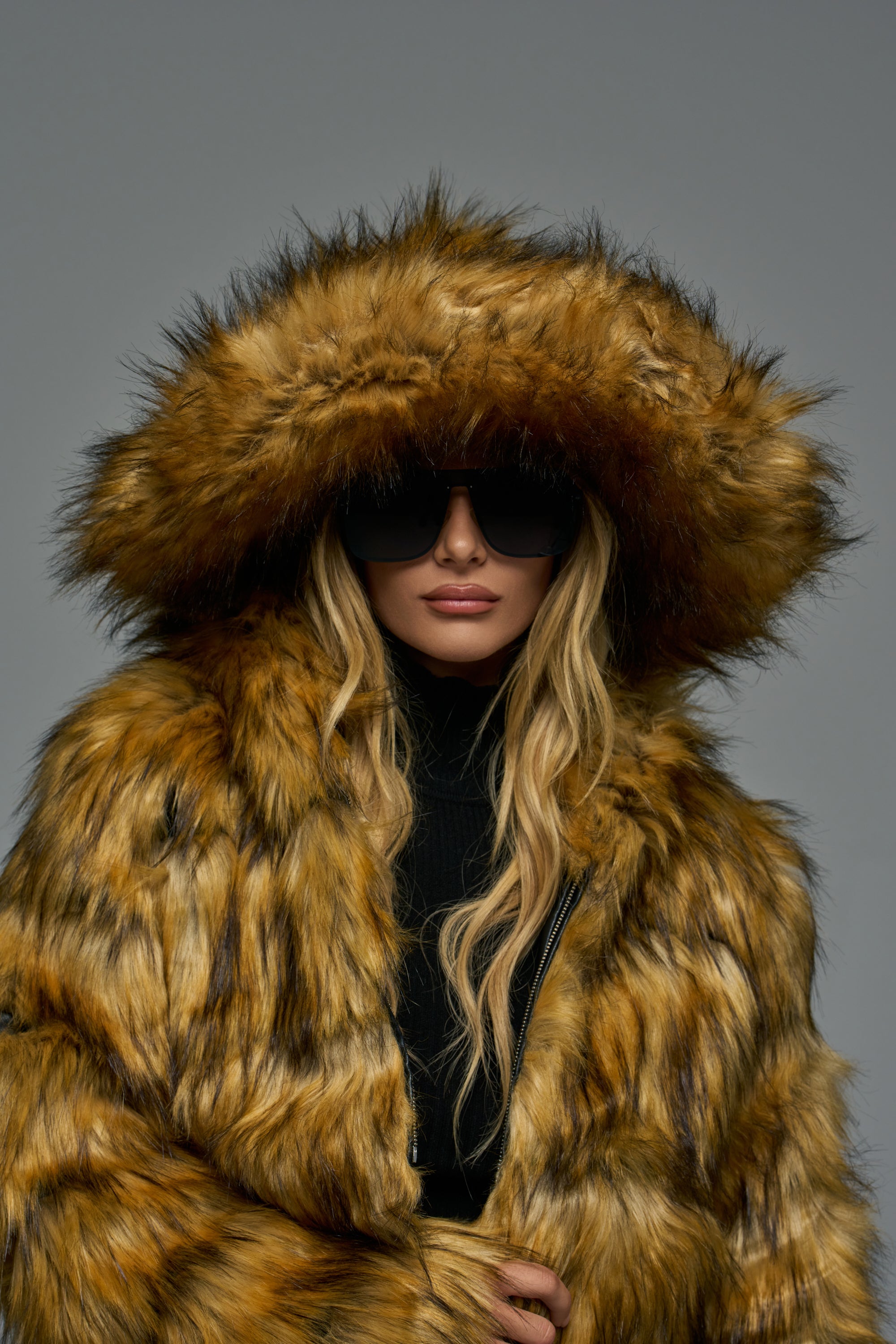 Person wearing an oversized faux fur hooded jacket, sunglasses, and a brown GRACELLE OVERSIZED FAUX FUR HAT as a winter accessory.