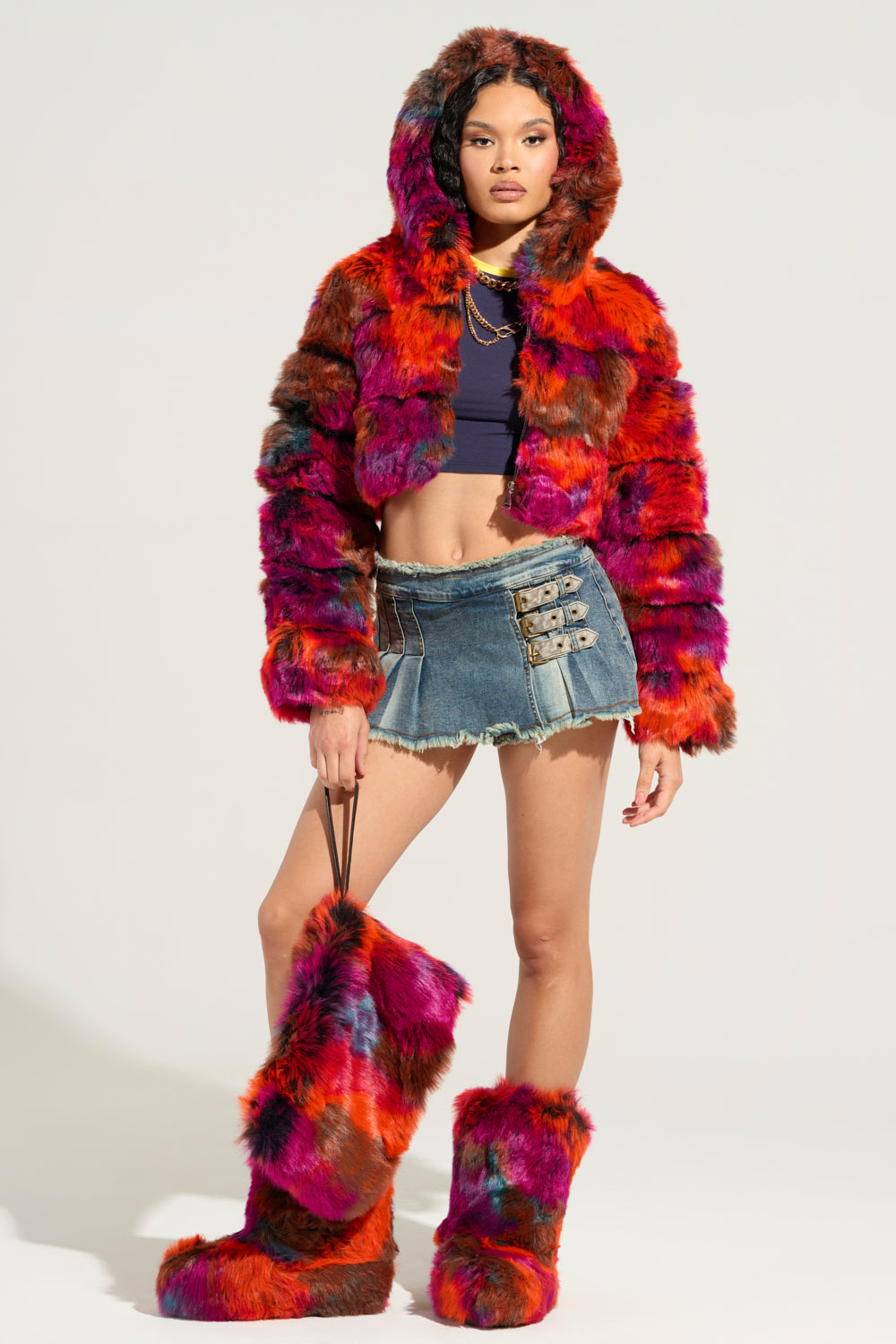 The outfit showcases the GRACELLE MULTI FAUX FUR CROPPED JACKET, paired with matching fur boots, a dark crop top, and a denim skirt featuring buckle details. The ensemble highlights bold colors such as red, pink, and orange with its vibrant design. 7