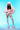 Dressed in the COTTON CANDY SKIES MULTI FAUX FUR BOMBER, a person strikes a confident pose against cotton candy skies. Their ensemble is completed with matching shorts, high platform shoes, and a vibrant faux fur hat. Long, curly hair and white lace thigh-high stockings add the perfect finishing touches to their look.