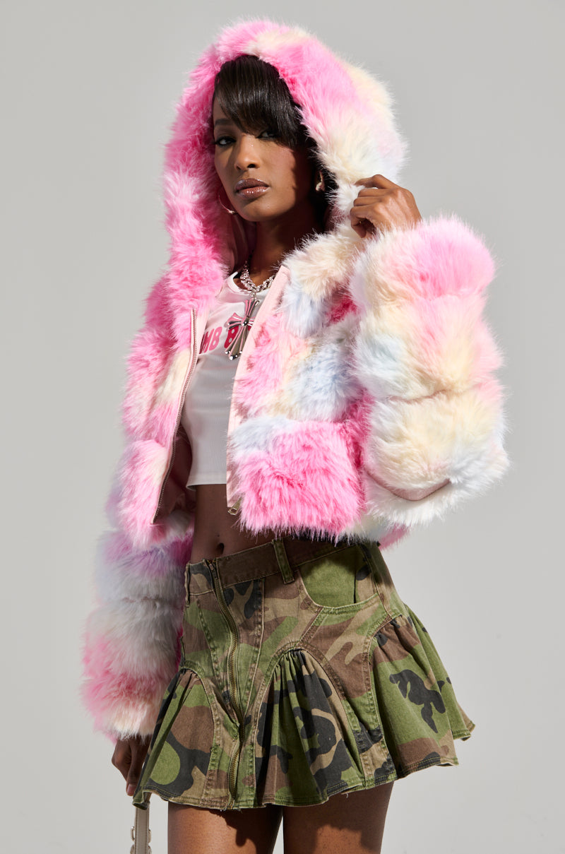 A person confidently poses against a simple background, wearing the COTTON CANDY SKIES MULTI FAUX FUR BOMBER, paired with a cropped white top and a camo-patterned skirt.
