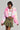 Dressed confidently in the COTTON CANDY SKIES MULTI FAUX FUR BOMBER paired with a white crop top and green camo skirt, they hold a white bag. Short hair and a necklace complete their look, standing against a background reminiscent of pastel cotton candy skies.