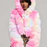 A person is striking a pose in the COTTON CANDY SKIES MULTI FAUX FUR BOMBER, showcasing vibrant shades of pink, white, and pastels. Paired with a camouflage-patterned skirt, the ensemble stands out brilliantly against the plain background.