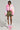 Dressed in the eye-catching COTTON CANDY SKIES MULTI FAUX FUR BOMBER, a person pairs their outfit with a white cropped hoodie, a camouflage mini skirt, and fuzzy rainbow boots. They stand against a plain background while holding a chic white handbag, perfectly embodying the whimsical essence of cotton candy skies.