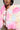 A person is wearing the COTTON CANDY SKIES MULTI FAUX FUR BOMBER, featuring shades of pink, blue, and yellow that evoke the look of cotton candy skies. They pair it with a white top and large hoop earrings. The image highlights their upper body, emphasizing the bomber's vibrant texture.