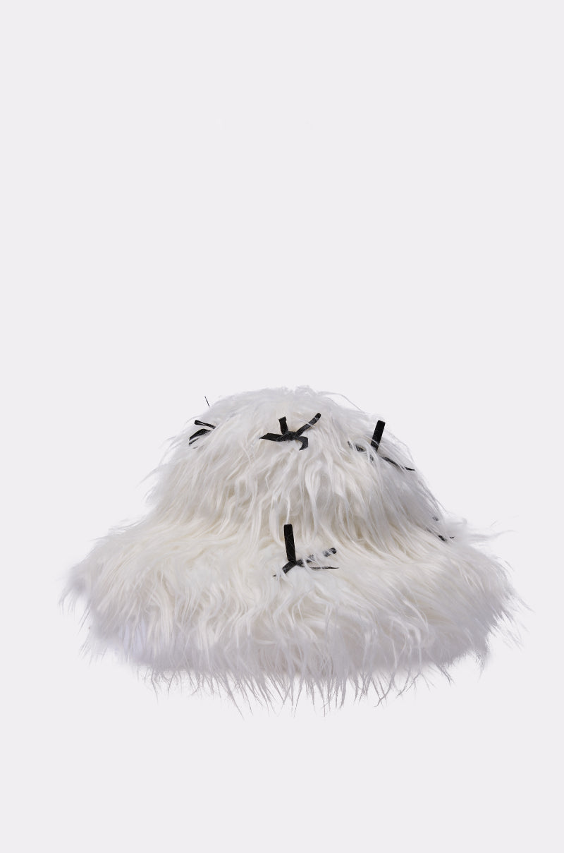 The WITH A BOW FAUX FUR BUCKET HAT is a white, shaggy faux fur bucket hat adorned with small black satin bows, making it the perfect coquette accessory against a simple light backdrop. 2