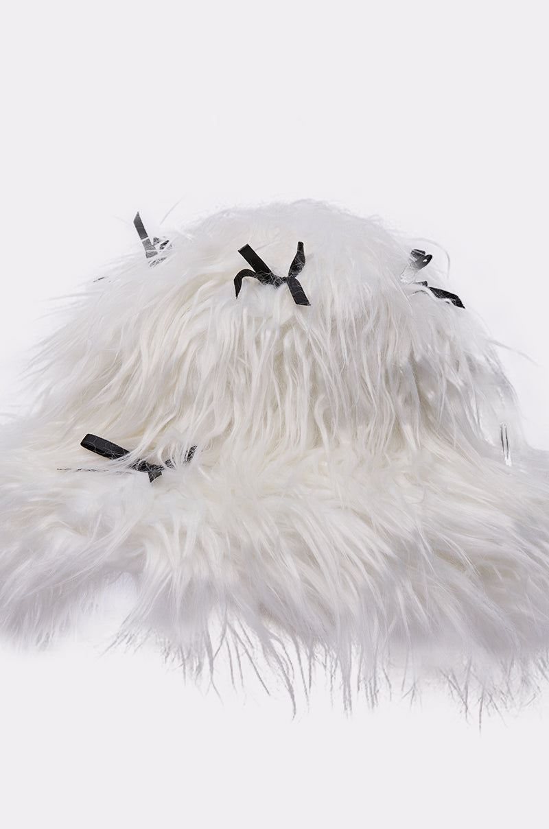 The WITH A BOW FAUX FUR BUCKET HAT features soft white faux fur and is decorated with small black satin bows, shown on a plain white background. 4