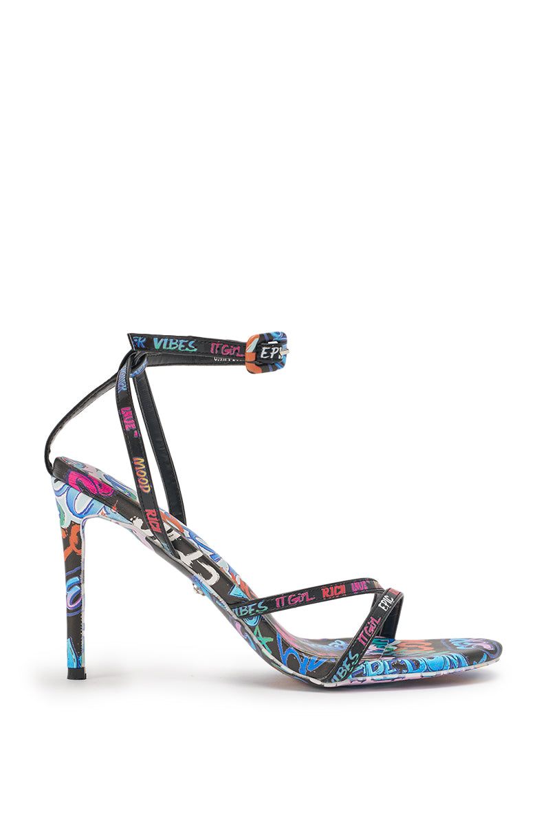 The AKIRA GOLD GRAFFITI PRINT STILETTO SANDAL features colorful urban-inspired graphics, delicate straps, an ankle buckle, and bold decorative artwork on the sole and heel for a standout party look. 3