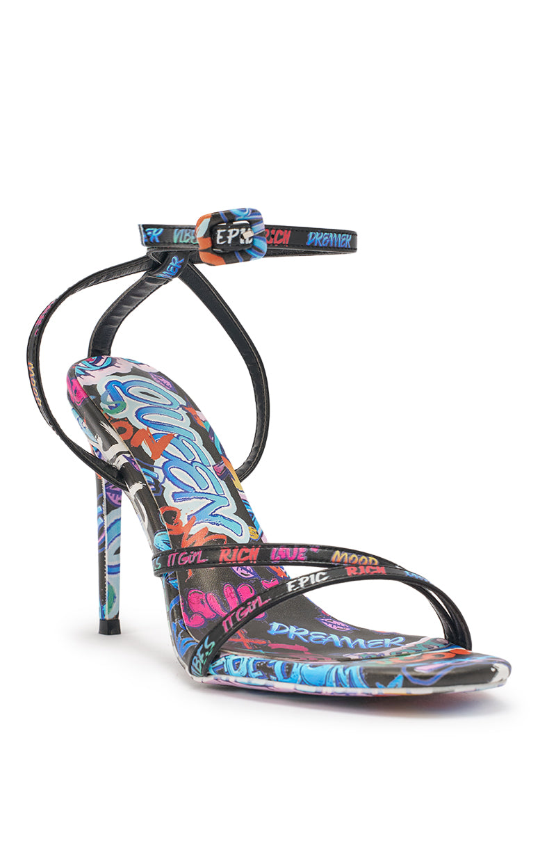 The AKIRA GOLD GRAFFITI PRINT STILETTO SANDAL features a strappy silhouette, thin ankle strap, open toe, and bold graffiti-inspired designs with colorful words and abstract patterns on the straps and sole—perfect for parties. 5