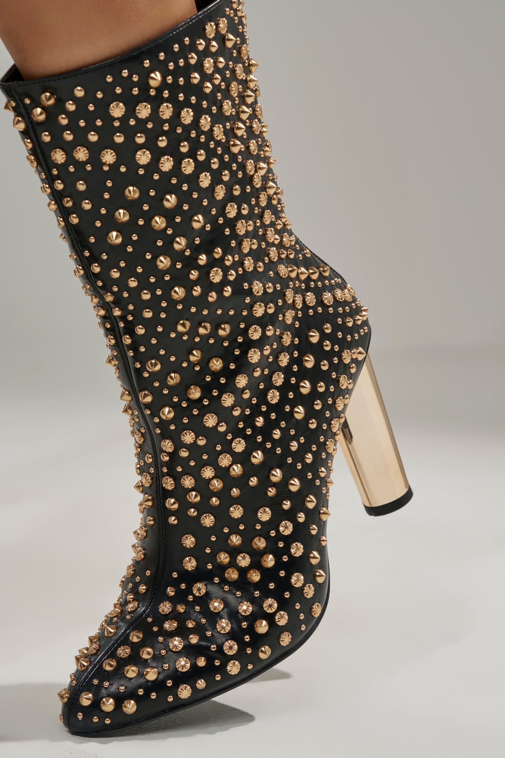 The AZALEA WANG GREHGAN BLACK EMBELLISHED CHUNKY HEEL BOOTIE features gold studs, a pointed toe, and a thick metallic gold heel. This edgy black bootie is shown against a plain background.