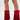 A person models the AZALEA WANG GREIA RED RHINESTONE COWBOY BOOTIE—sparkly red, faux suede booties with fringe and pointed toes—against a white background, revealing part of a leg tattoo above the left boot.
