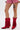 Wearing red, checkered shorts and AZALEA WANG GREIA RED RHINESTONE COWBOY BOOTIE with faux suede details, a person with a skull-in-heart thigh tattoo stands against a plain white background.