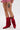 A person wearing the AZALEA WANG GREIA RED RHINESTONE COWBOY BOOTIE stands with one leg forward, showing off a thigh tattoo of a skull in an ice cream cone, paired with a red and white checkered skirt.