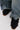 A close-up of someone in wide-legged, faded blue jeans wearing AZALEA WANG GREYI BLACK PUFF FLORAL FLAT SNEAKERS adorned with fabric pom-poms, standing on a light-colored surface.