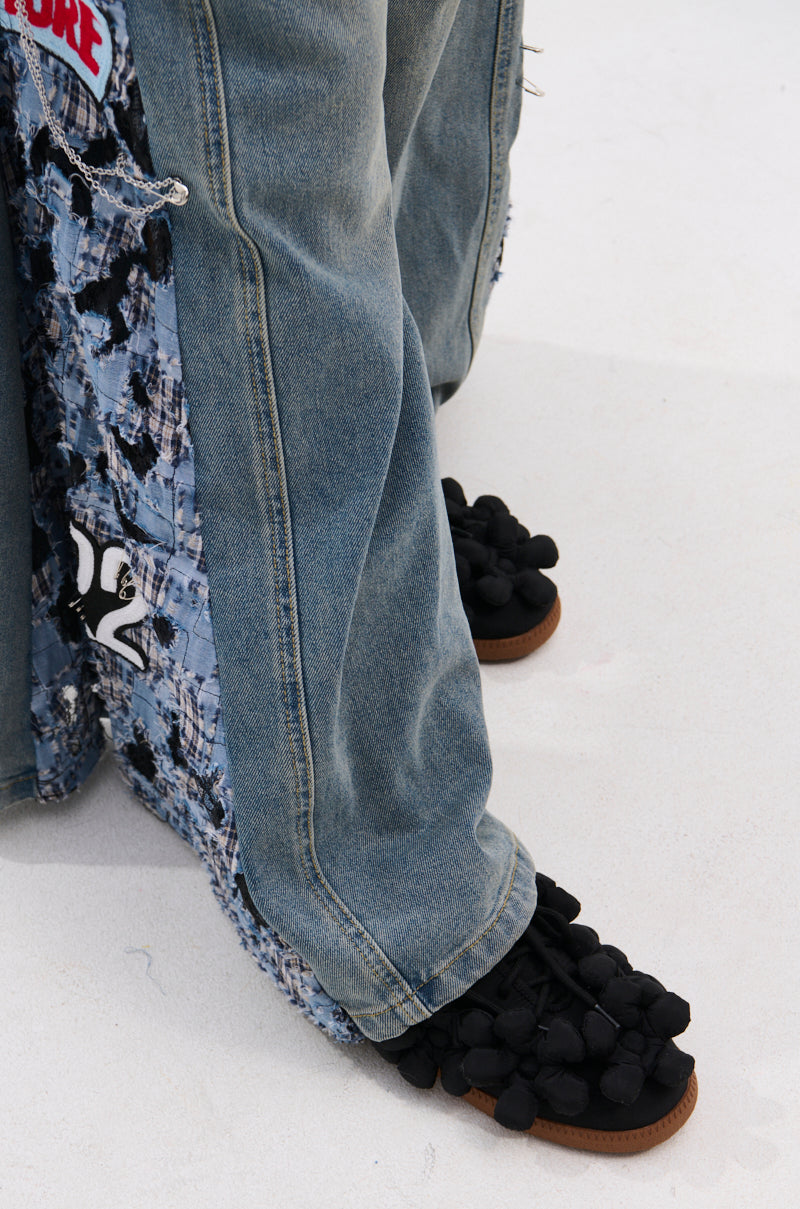 A person stands on a light surface wearing wide-legged patchwork jeans and AZALEA WANG GREYI BLACK PUFF FLORAL FLAT SNEAKERS.