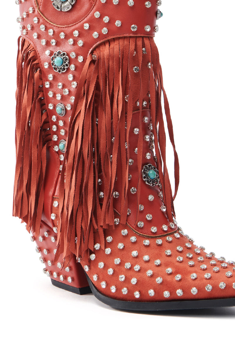 The AZALEA WANG GREYSON RED BOOT features a western-inspired design with red faux suede, silver studs, turquoise flower accents, and long fringe. It boasts a pointed toe and angled heel adorned with rhinestone studs.