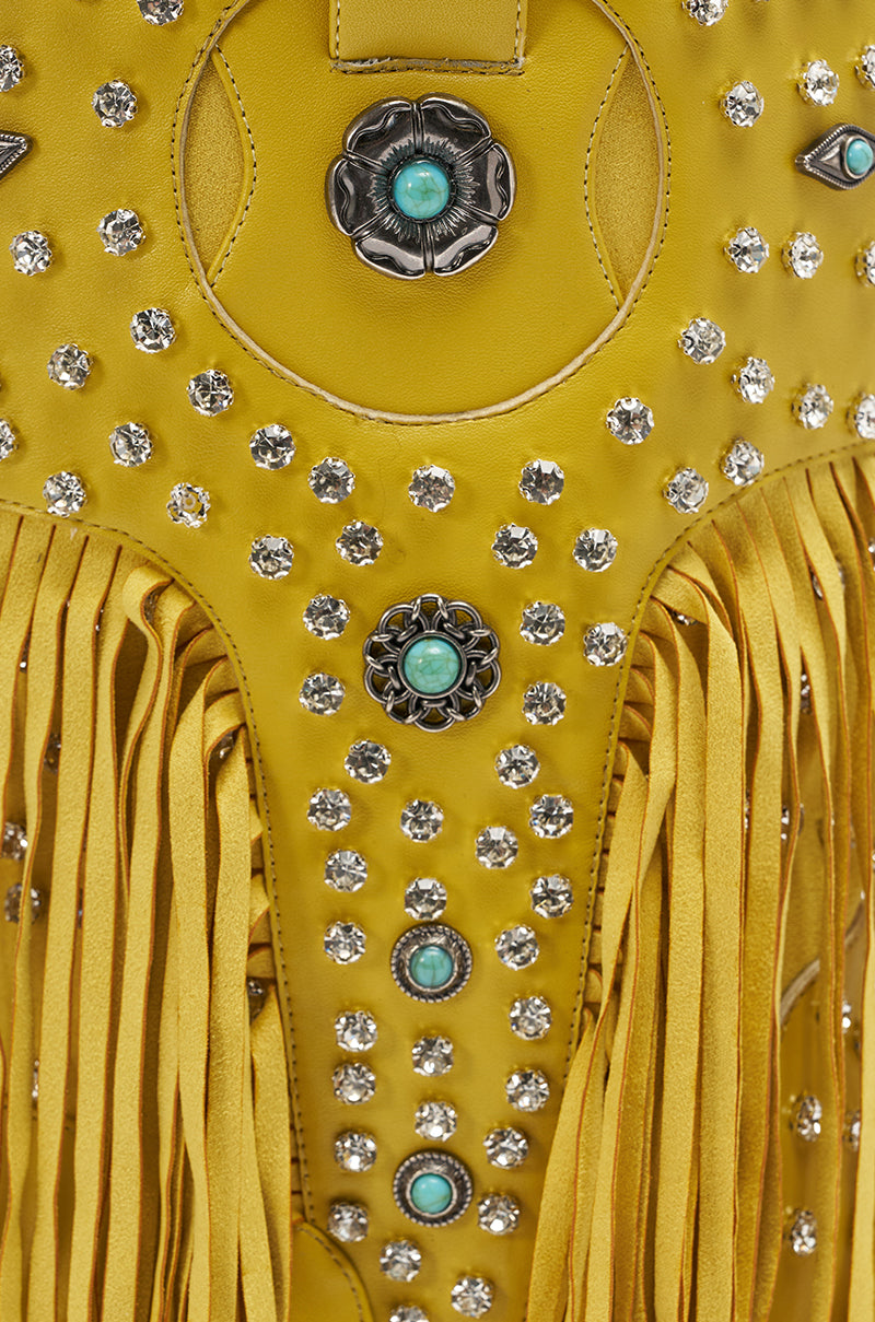 Close-up of the AZALEA WANG GREYSON YELLOW RHINESTONE EMBELLISHED WESTERN BOOTIE, featuring silver studs, turquoise floral metal accents, clear rhinestones, yellow faux leather, and long fringe for a bold Western-inspired style.