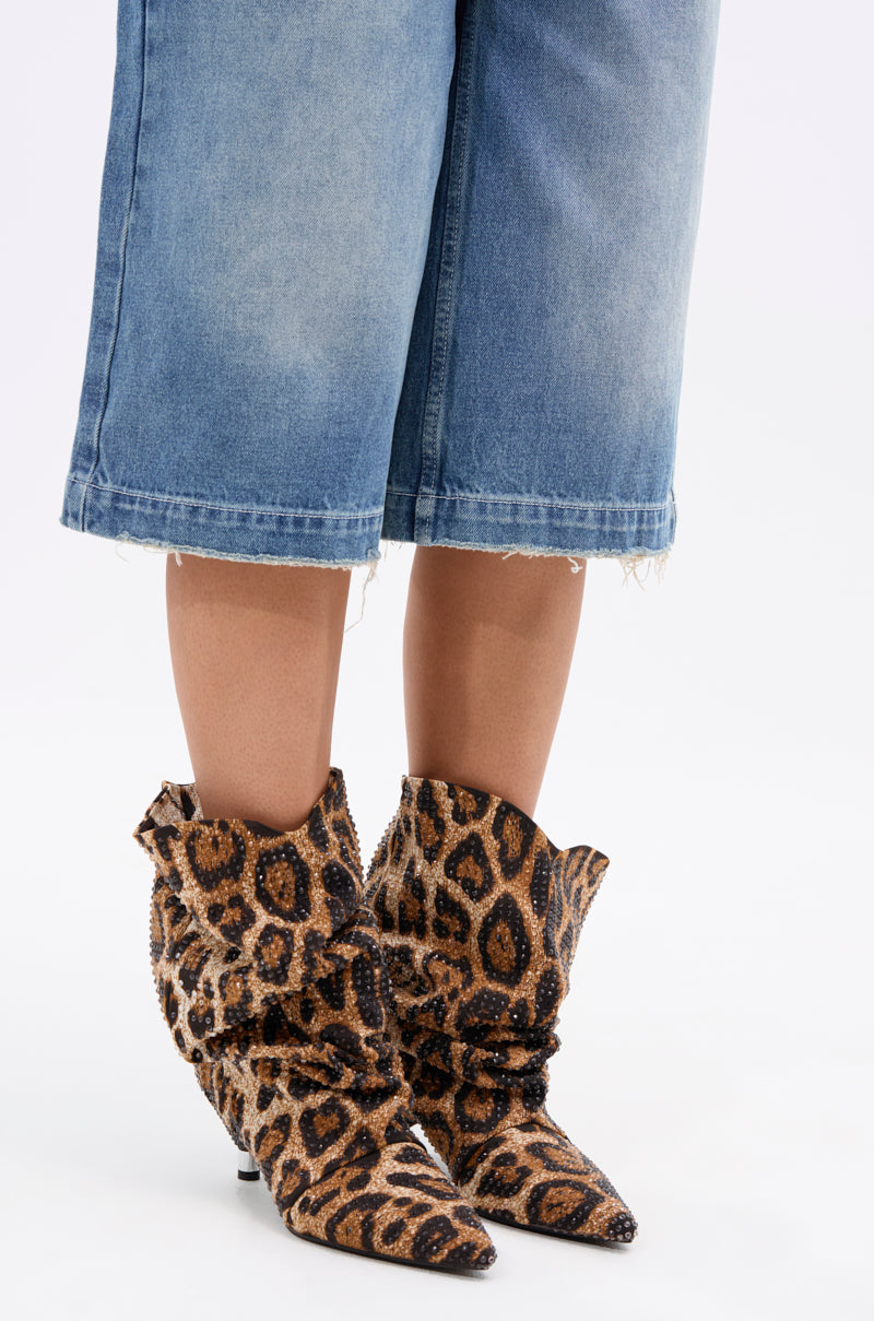 A person in mid-length, frayed hem denim shorts and AZALEA WANG GRIMES LEOPARD STILETTO BOOTIE with a brown and black pattern stands against a white background.