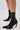 Someone stands on a light surface wearing the AZALEA WANG GRYFFON BLACK STILETTO BOOTIE, featuring faux leather, a side zipper, and multicolored beaded heels with rainbow spike studs.