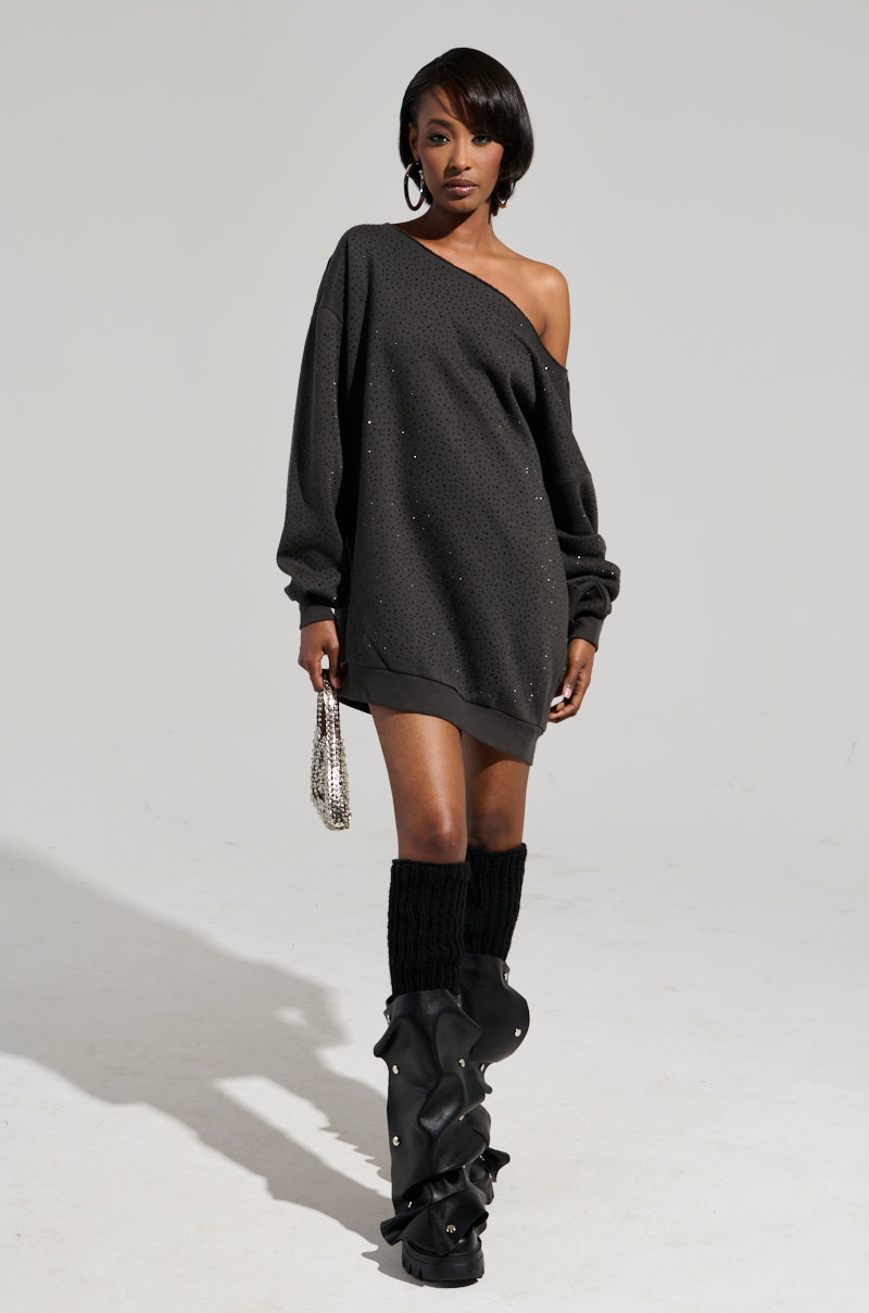 Dressed in a STREET STYLE OVERSIZED RHINESTONE SWEATSHIRT DRESS, the individual confidently holds a small handbag while wearing knee-high leg warmers and chunky boots, perfectly capturing the relaxed fit against a simple backdrop.