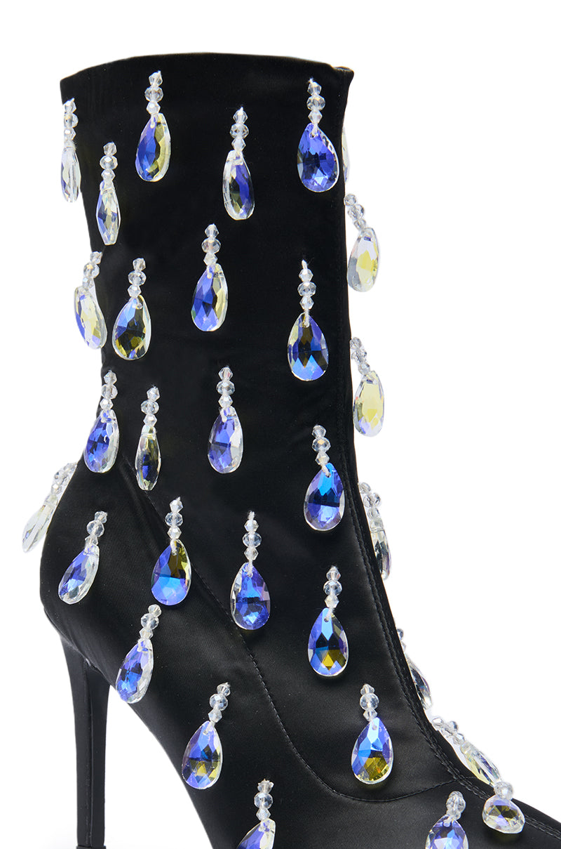The AZALEA WANG GUANTLETT BLACK CRYSTAL EMBELLISHED BOOTIE is an ankle-high black bootie with a stiletto heel, decorated with large teardrop-shaped blue and yellow rhinestones for striking sparkle.