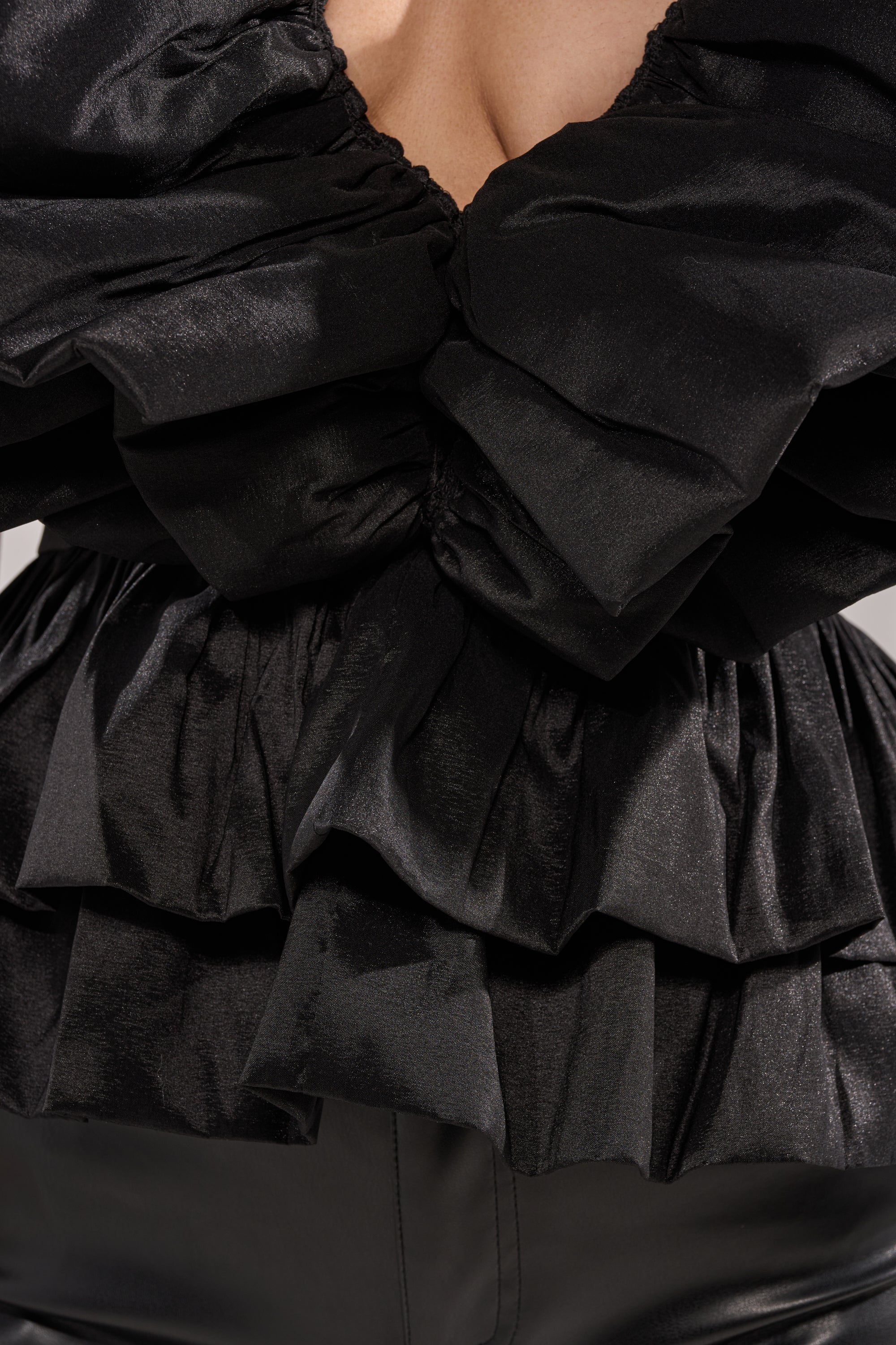 Close-up of a person wearing the WORK OF ART BLOUSE—a black, ruffled organza top with layered details—paired with black leather pants. Only the torso is visible, highlighting statement eveningwear style. 5