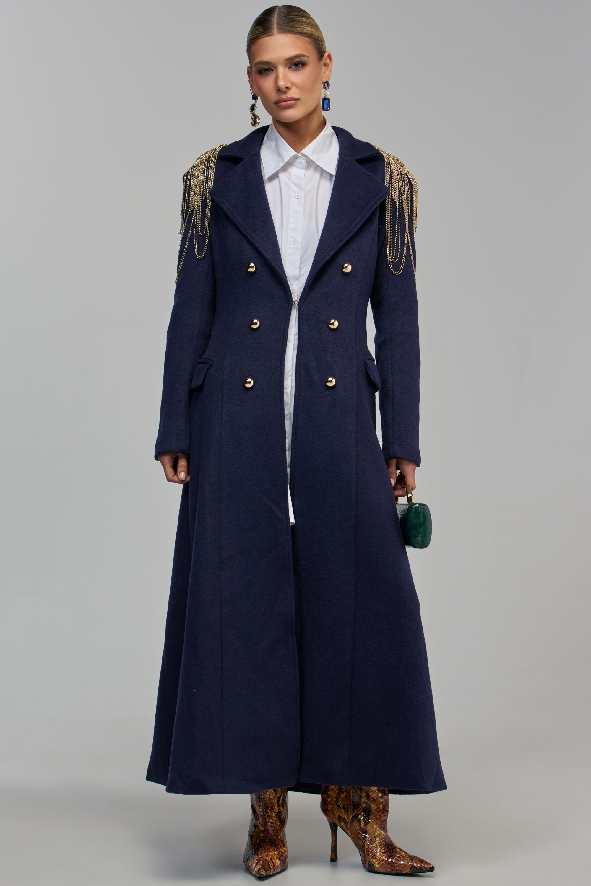 A person wears the FOLLOW MY LEAD MILITARY TRENCH in navy with rhinestone epaulettes, styled with a white button-down shirt and snakeskin-print heeled boots.