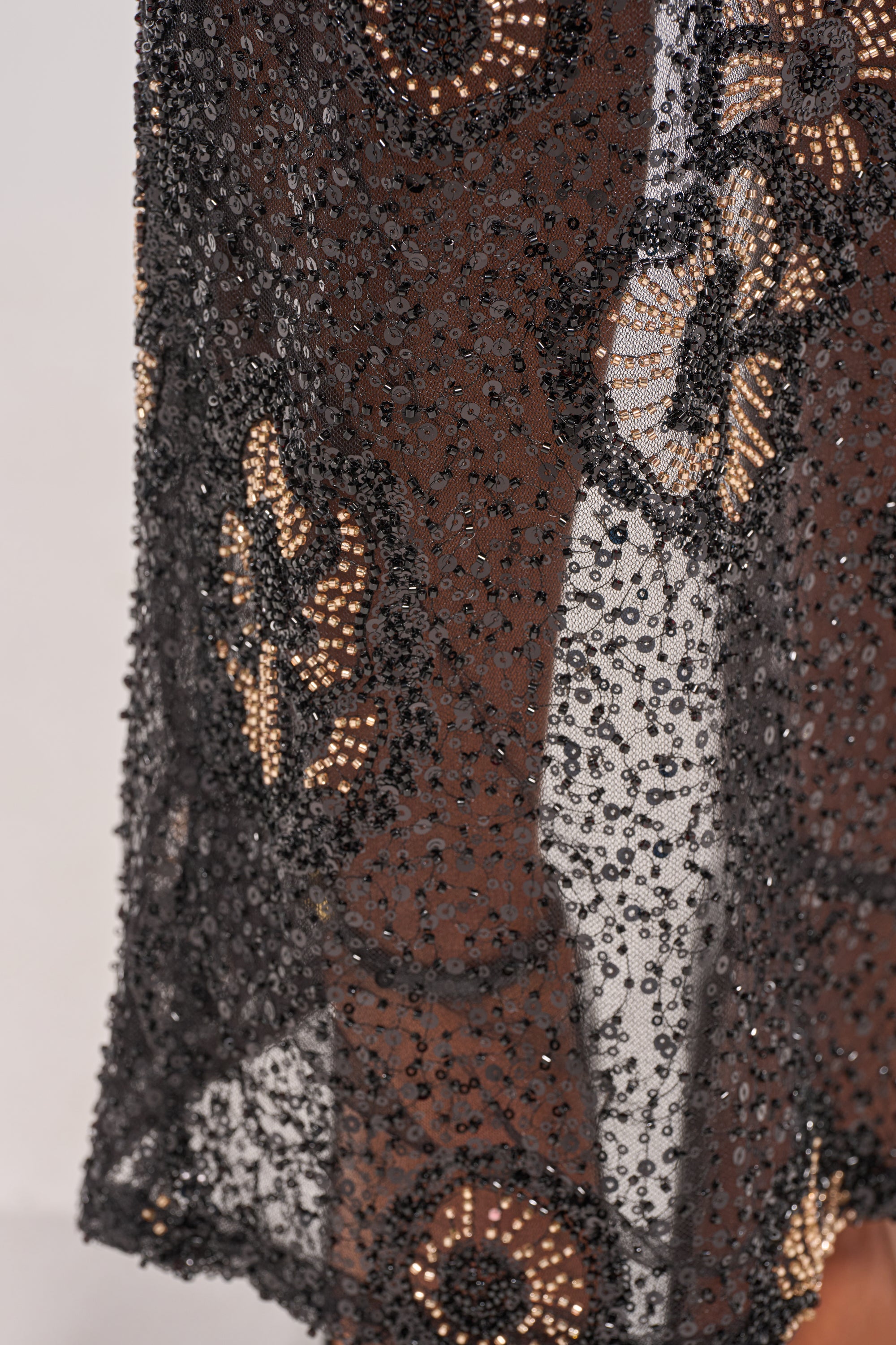 Close-up of the ALL EYES ON ME FLORAL MAXI SKIRT featuring sheer black fabric with sequin floral embroidery and sparkling black beads, revealing a light skin tone underneath. 8