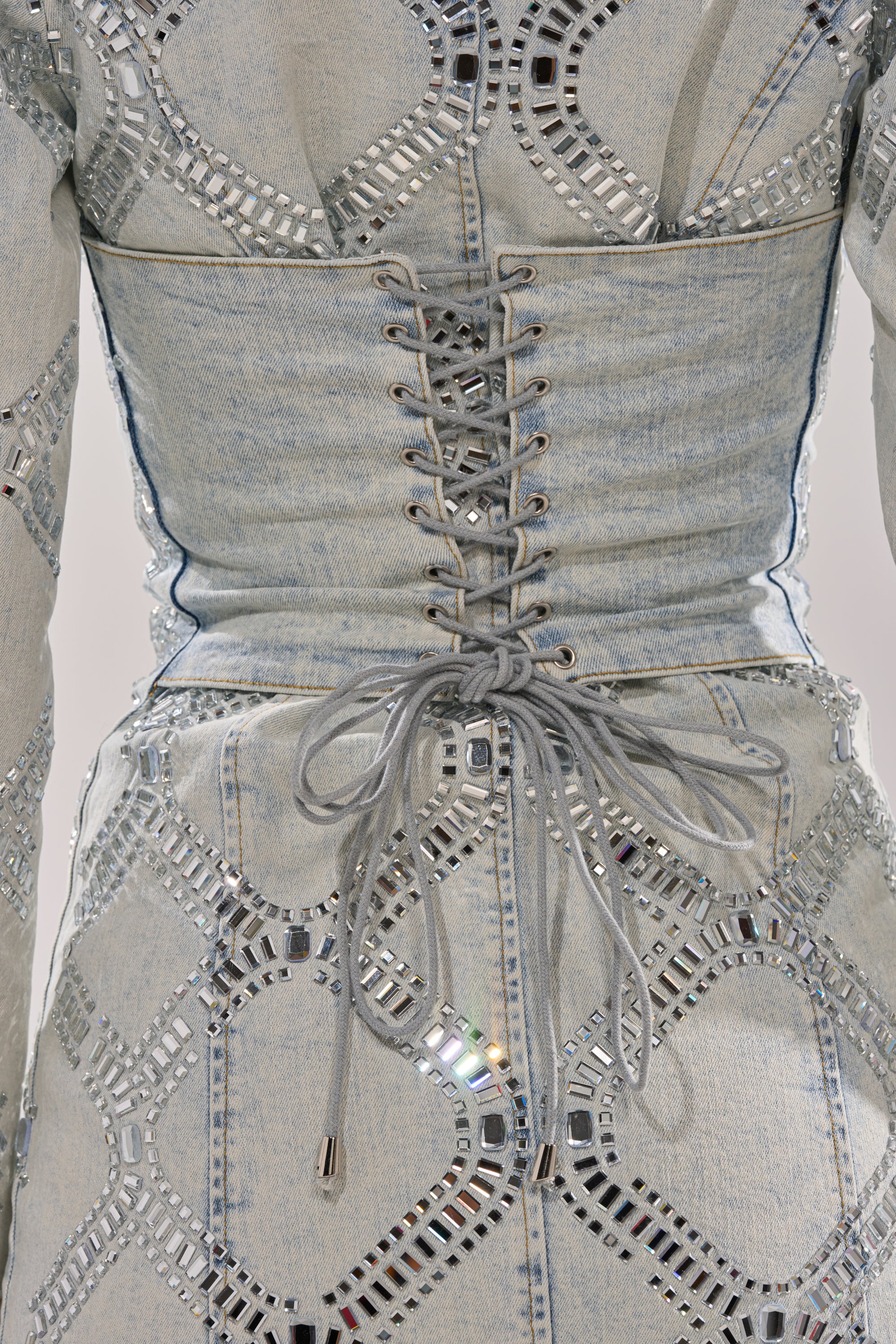 Close-up of the LOOK AT ME RHINESTONE BLAZER DRESS IN LIGHT BLUE DENIM, featuring geometric silver rhinestone embellishments and a corset-style lace-up back tied in a bow at the waist.