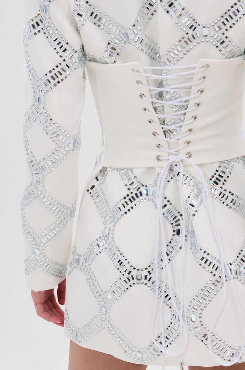 A close-up of a person wearing the LOOK AT ME RHINESTONE BLAZER DRESS IN WHITE, featuring satin lining, a lace-up corset back, and silver geometric rhinestone patterns in a grid design.
